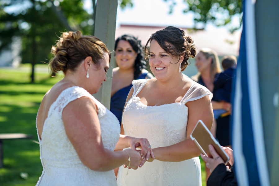 Two brides exchange wedding rings during their outside ceremony.